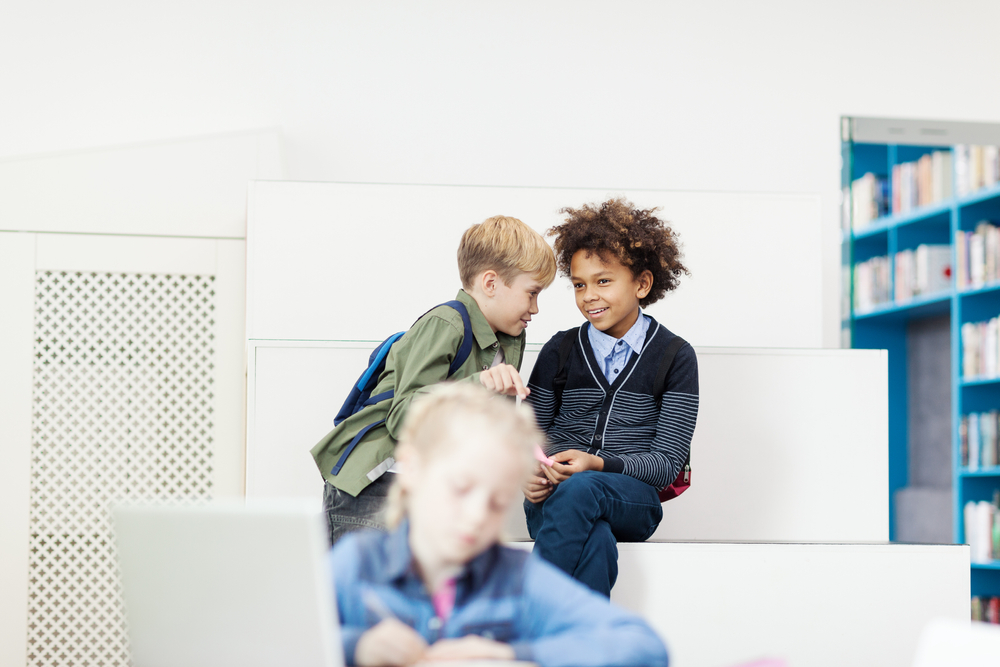 Two,diverse,boys,gossiping,about,schoolgirl,sitting,at,desk,in